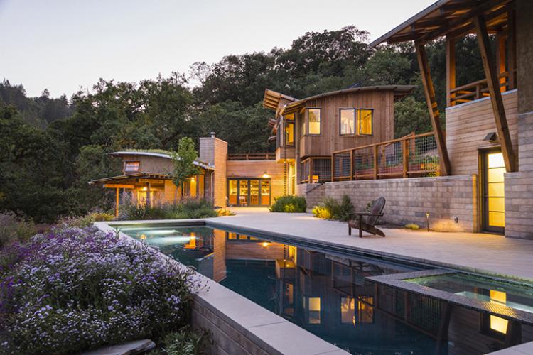 Watershed straw-bale residence at dusk with pool and decks